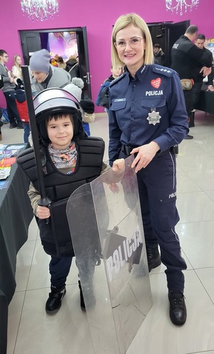 Policjantka pozuje do zdjęcia razem z chłopcem ubranym w sprzęt przeciwuderzeniowy.